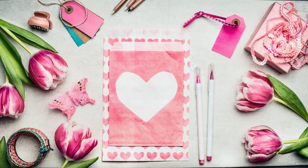 Springtime womens workspace with pink tulips flowers, paper envelope with heart, brush markers, tags and gift box, top view, copy space. Gift and greeting card making for Mothers Day - Fotografie, Obrázek
