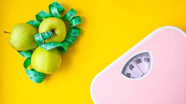 Zelené jablko s měřicí páskou a růžovými váhovými stupnicemi. Pojetí zdravotní péče, fitness doma, strava - Fotografie, Obrázek