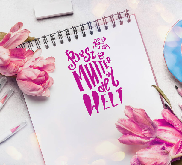 Mothers Day Greeting card with text lettering in german Beste Mutter der Welt , pale pink  tulips, notebook or sketchbook and colorful brush markers ,  top view - Fotoğraf, Görsel