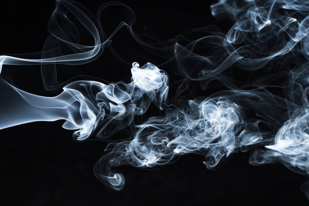 Background image of a wisp of smoke on a dark background. The texture of the flowing smoke. Frozen smoke on a dark background. Graphic resources dark backdrop. Texura of white clouds of fog. Curls of smoke frozen in motion. - 写真・画像