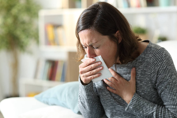 Sick adult woman coughing covering mouth with tissue sitting on a couch at home - Foto, Bild