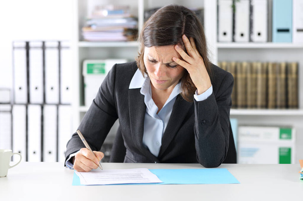 Hesitant mujer ejecutiva adulta dudando de firmar contrato sentado en un escritorio en la oficina
 - Foto, imagen