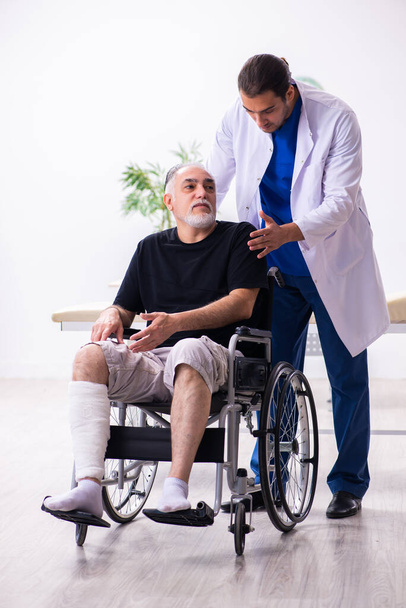 Γέρος τραυματίας άνδρας που επισκέπτεται νεαρό άνδρα γιατρό τραυματολόγο - Φωτογραφία, εικόνα