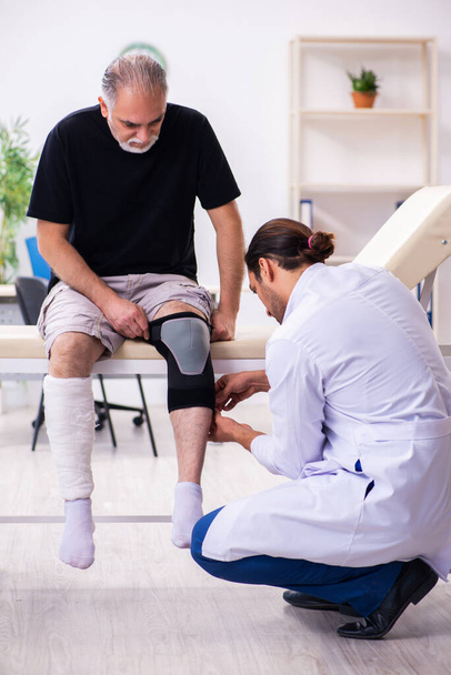 Old injured man visiting young male doctor traumatologist - Foto, Bild