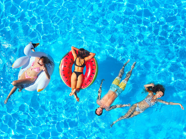 Aerial of friends having party in swimming pool with inflatable flamingo, swan, mattress. Happy young people relax at luxury resort on sunny day. View from above. Girls in bikini sunbathing in a sun. - Fotó, kép