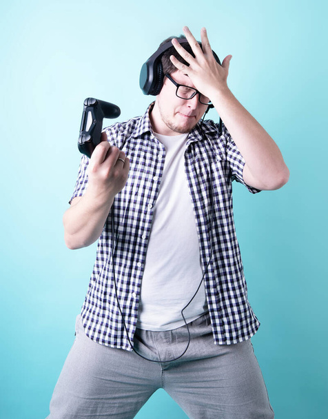 Сиди дома. Разочарованный молодой человек играет в видеоигры держа джойстик изолирован на синем фоне
 - Фото, изображение