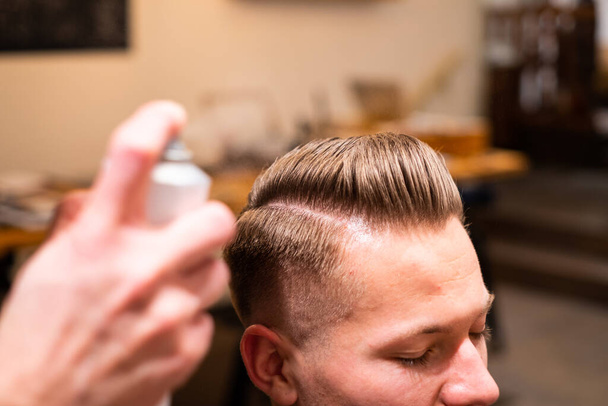 Peluquería rocía el cabello de un joven con laca después de cortarse el pelo en su barbería
 - Foto, imagen