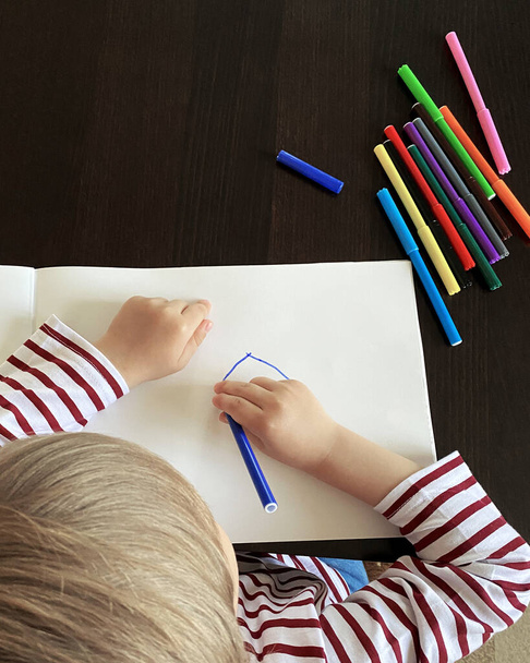 Small boy draws at the table. Top view, felt-tip pens of different colors are on the table - Fotoğraf, Görsel