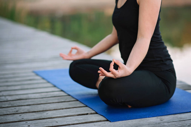 woman doing yoga in lotus position outdoors near the river on a wooden pier in the morning. Healthy lifestyle concept. Morning meditation, relaxation. - Photo, Image