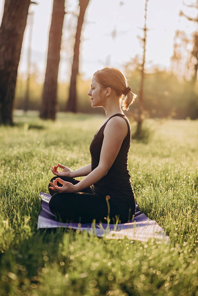 36-letnia młoda kobieta ćwiczy jogę rano w lesie wśród drzew w pozycji lotosu. Koncepcja zdrowego stylu życia. Poranna medytacja, relaks. Miękkie ukierunkowanie selektywne. - Zdjęcie, obraz