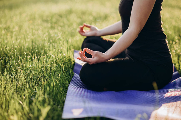 Jonge blanke vrouw beoefent yoga in lotuspositie op een vroege zonnige ochtend in een bos. Gezond levensstijl concept. Ochtendmeditatie, ontspanning. Zachte selectieve focus. - Foto, afbeelding