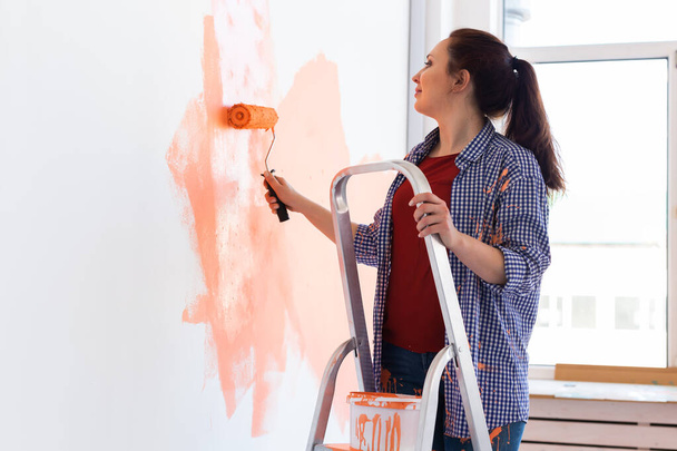 Счастливая молодая женщина красит внутреннюю стену с краской роликом в новом доме. Женщина с роликом наносит краску на стену
. - Фото, изображение