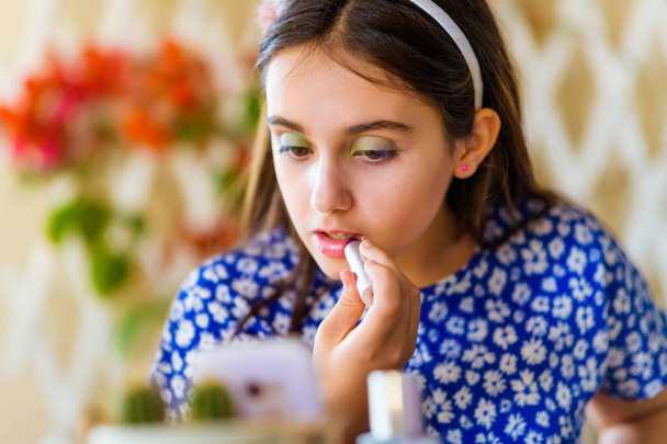 Attractive young girl following an online makeup course on her smartphone applying lipstick or gloss to her lips in a close up cropped portrait - Photo, Image