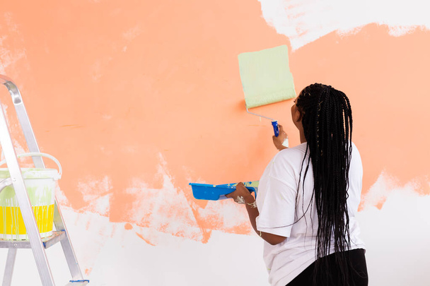 Επισκευή στο διαμέρισμα. Ευτυχισμένη νεαρή γυναίκα ζωγραφίζει τον τοίχο με μπογιά.. - Φωτογραφία, εικόνα