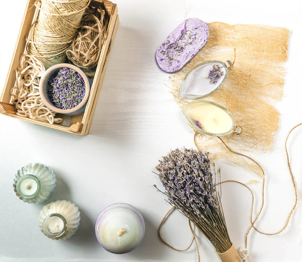Flat lay composition of handmade soap bar with dried lavender flowers, purple and cream Candles on a white background with a wooden texture. Lavender flowers and wooden accessories in a wooden box in - Foto, Bild