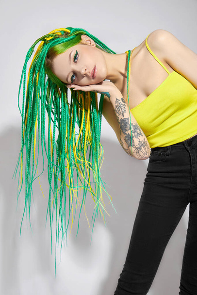 Portrait of a woman with creatively colored hair in green and yellow color. Colorful bright dreadlocks, beautiful modern makeup - Foto, Imagem