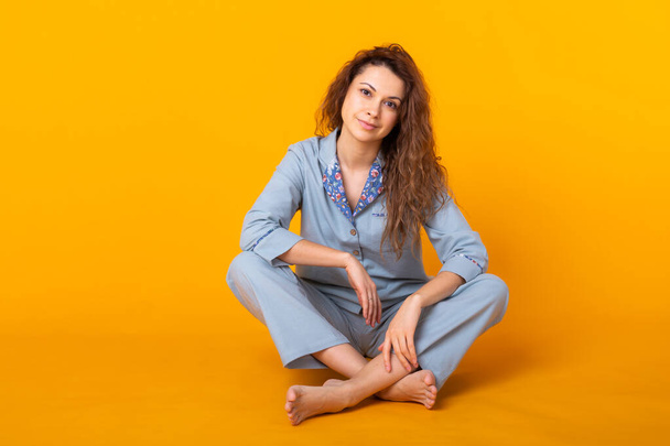 Usmívající se mladá dívka v pyžamu domácí oblečení pózovat zatímco odpočívá doma izolované na žlutém pozadí studiového portrétu. Relax dobrý nálada životní styl koncept. - Fotografie, Obrázek