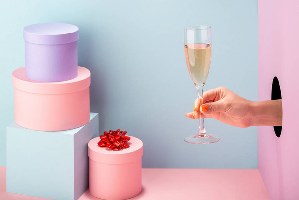 Womans hand holding a glass of white wine on blue and pink background - Fotó, kép