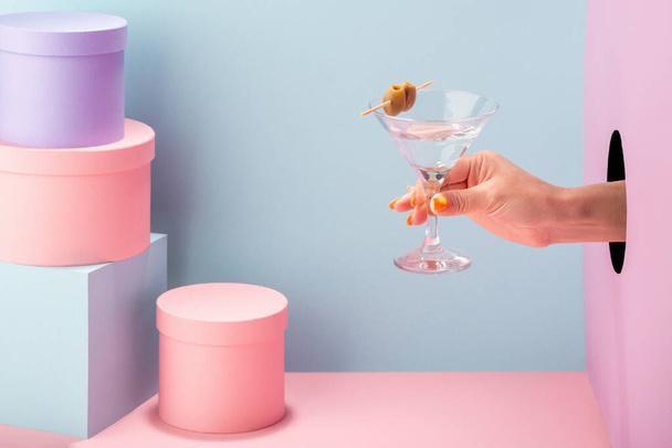 Womans hand holding a glass of cocktail on blue and pink background - Fotó, kép