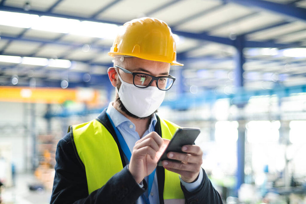 Technician or engineer with protective mask and telephone in industrial factory. - Photo, image