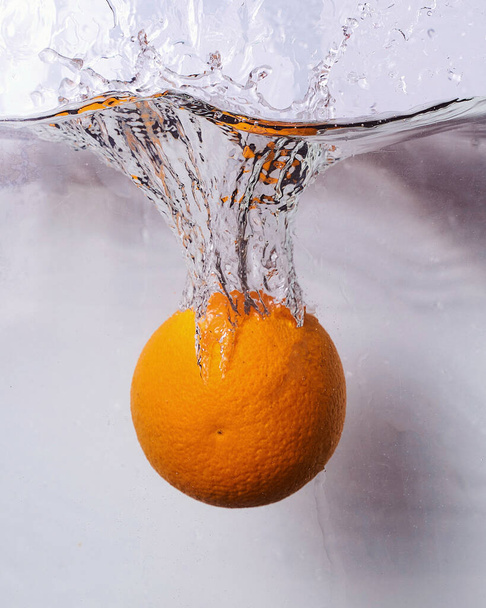 Naranja cayendo al agua y creando salpicaduras
 - Foto, imagen