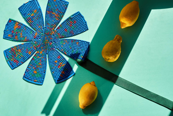Композитная рамка с синим массажером в форме цветка на зеленом фоне и лимонов, с лентами солнца и тени. Вид сверху, плоский. Реклама, тематическая и тематическая съемка. Для отдыха и здоровья
 - Фото, изображение