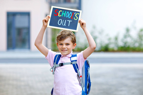 Happy little kid boy with backpack or satchel. Schoolkid on the way to school. Healthy adorable child outdoors With chalk desk for copyspace. Back to school or schools out. - Photo, Image