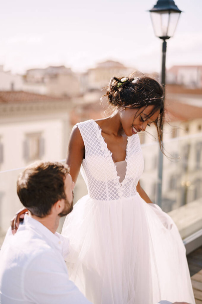 Casamento de arte de destino em Florença, Itália. Casamento multiétnico. Noiva afro-americana e noivo caucasiano estão dançando perto da mesa para um jantar de casamento, no telhado do restaurante
. - Foto, Imagem
