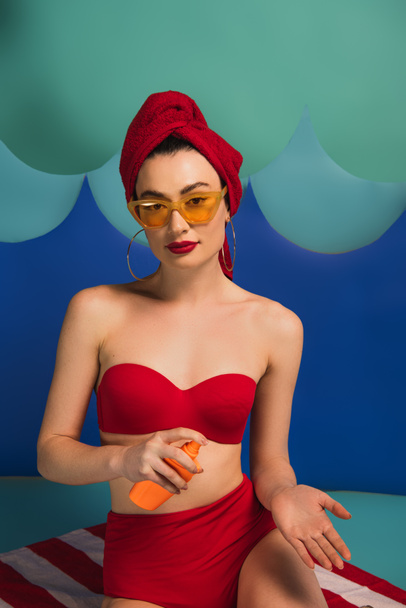 atractiva mujer en traje de baño rojo y gafas de sol sosteniendo protector solar cerca de las ondas de corte de papel
  - Foto, Imagen