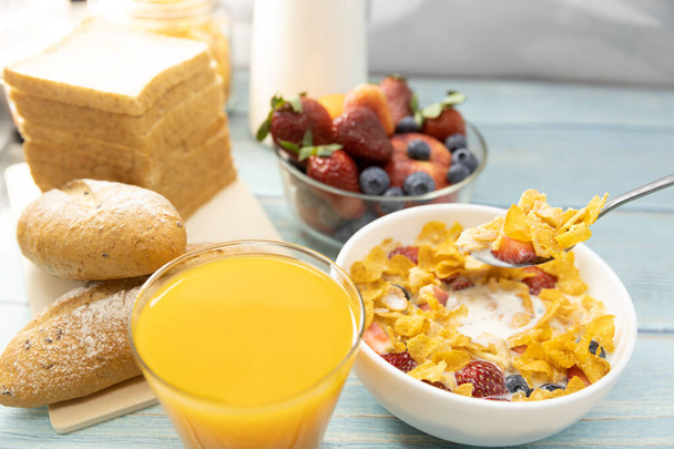 Gezond ontbijt. brood, sinaasappelsap, aardbeien, bosbessen, melk en ontbijtgranen in kom op houten tafel. Gezond voedsel - Foto, afbeelding