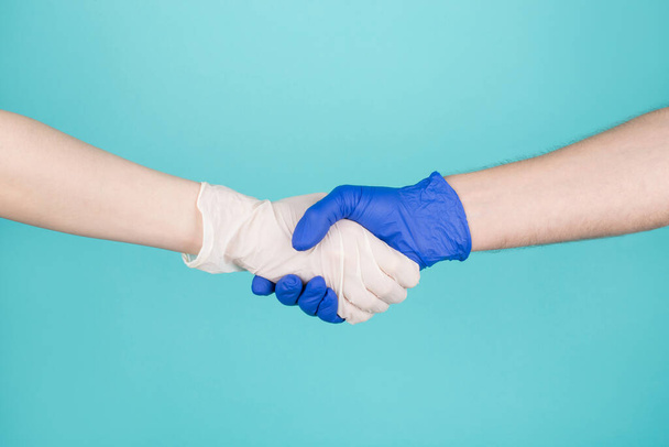 Koncepcja spotkania lekarzy i pacjentów. Koncepcja. Przycięte zbliżenie zdjęcie kobiety i mężczyzny w rękawiczkach witają się uściskiem dłoni odizolowanych na turkusowym niebieskim białym tle - Zdjęcie, obraz