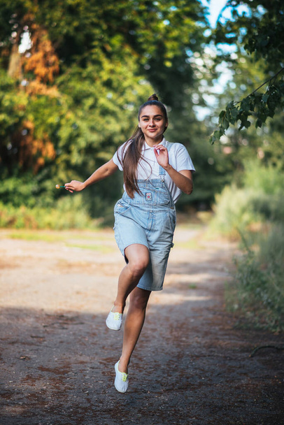 A girl in denim overalls smiles and runs outdoors. For any purpose. - Foto, Bild