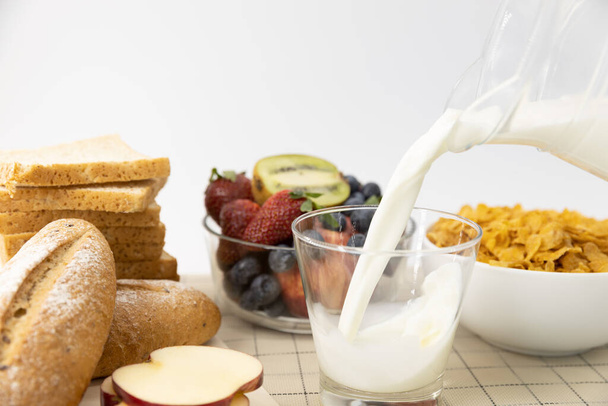 Close up Milch in Glas auf Hintergrund gießen Gesundes Frühstücksbrot, Erdbeere, Blaubeeren, Kiwi und Müsli in Schüssel. Gesunde Ernährung - Foto, Bild