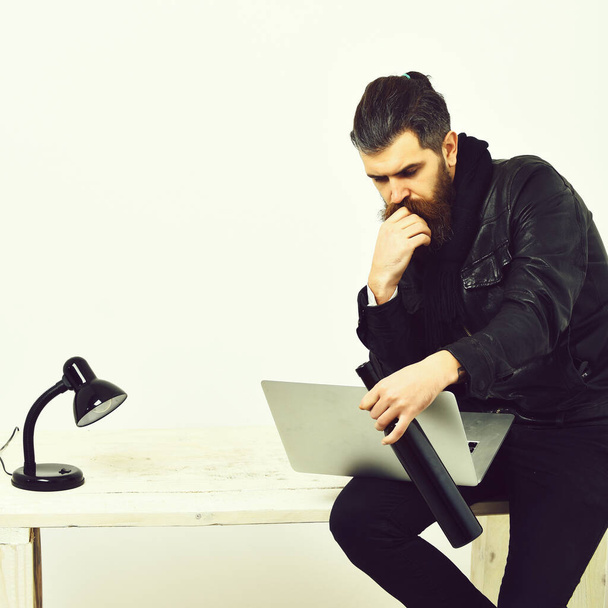 Bearded brutal caucasian hipster sitting on table with laptop - Fotó, kép