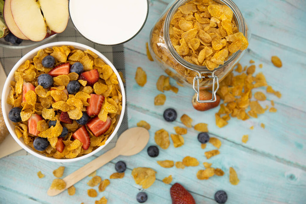 Gesundes Frühstück. Brot, Obst, Erdbeeren, Blaubeeren, Kiwi, Milch im Glas und Müsli in Schale auf Matte und Holztisch. Hintergrund Gesunde Ernährung. - Foto, Bild