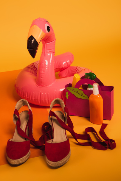 sac en papier avec crème solaire dans des bouteilles près de l'anneau gonflable rose et des chaussures de plate-forme sur jaune
 - Photo, image