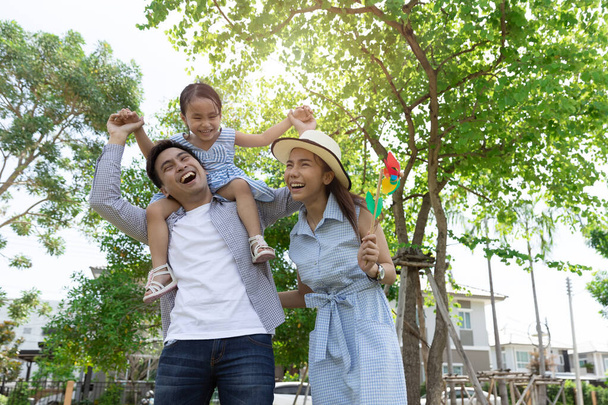Szczęśliwa azjatycka rodzina. Ojciec oddał córkę na barana w parku, w naturalnym słońcu, w tle i w domu. Koncepcja rodzinnych wakacji z przestrzenią do kopiowania - Zdjęcie, obraz
