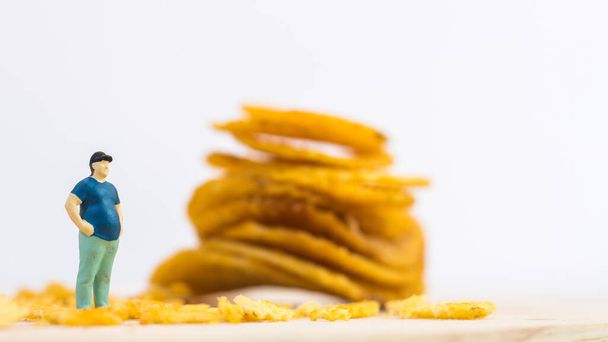 Miniatuur mensen, Close-up dikke man naast chips op witte achtergrond (food concept) - Foto, afbeelding