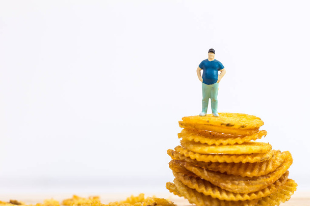 Miniaturní lidé, Tlustý muž stojící na bramborových lupíncích na bílém pozadí (jídlo koncept) - Fotografie, Obrázek