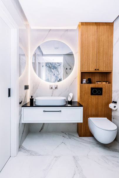 Moderno baño de lujo nuevo. Diseño interior con mármol, madera y acero inoxidable. Espejo redondo con luz led detrás
 - Foto, Imagen