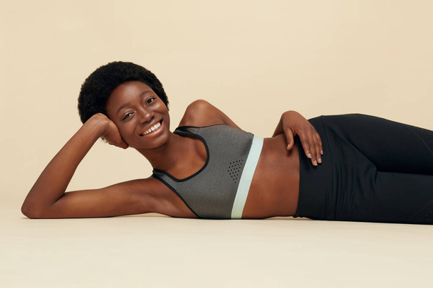 Fit Girl. Sporty African Woman Portrait. Smiling Female In Sportswear Lying Leaning On Hand. Beautiful Model Relaxing On Floor After Exercising. Fitness For Active Lifestyle. - Zdjęcie, obraz