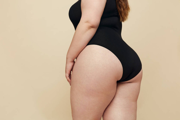 Plus Size Model. Woman Hips Close Up. Fat Torso In Black Bodysuit. Full-figured Female Posing On Beige Background. Body Positive Concept. - Zdjęcie, obraz