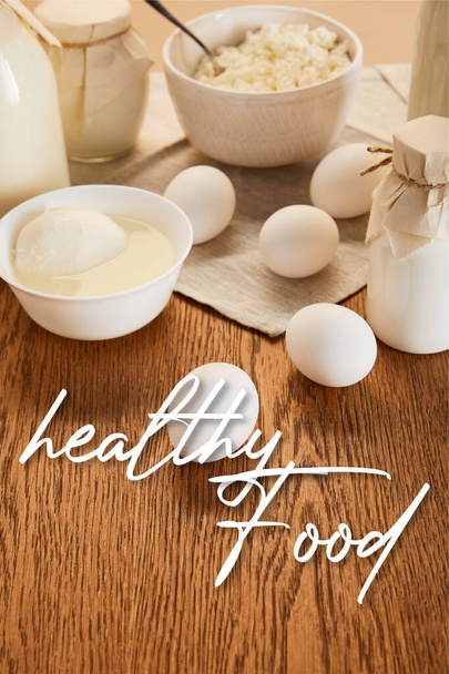 Selektiver Fokus verschiedener frischer Bio-Milchprodukte und Eier auf rustikalem Holztisch mit gesunder Lebensmittelillustration  - Foto, Bild