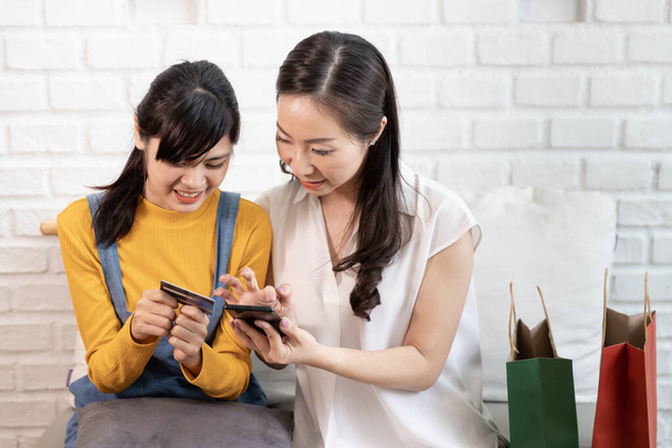 Boldog ázsiai család Anya és tizenéves lánya használ okos telefon Online vásárlás hitelkártyával egy szobában a természet napfény a házban. Vásárlás otthon koncepció - Fotó, kép
