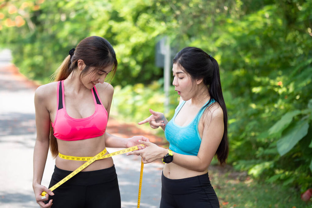 Dvě štíhlé krásné asijské mladá žena ve sportovním oblečení jsou měření její tenký pas s páskou opatření. hubnutí cvičením, dobrý zdravotní koncept. - Fotografie, Obrázek
