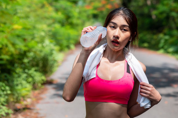 Після бігу красиві азіатські жінки п "ють воду з пляшки. Вранці в саду. Здорова питна вода і розважність - Фото, зображення