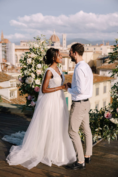 Mezirasový svatební pár. Svatební obřad na střeše budovy s výhledem na město a katedrálu Santa Maria Del Fiore. Cílová výtvarná svatba ve Florencii, Itálie - Fotografie, Obrázek