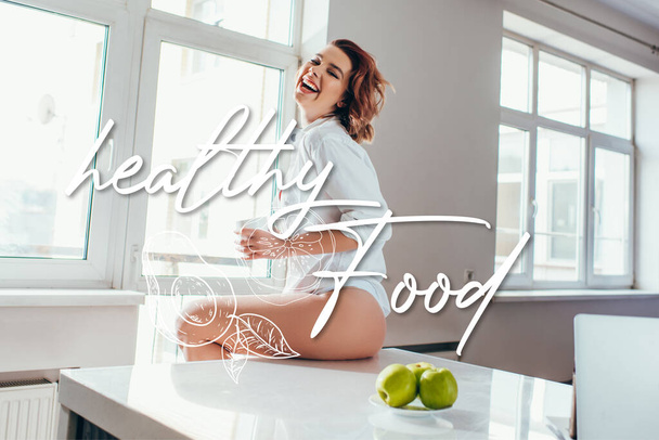 cheerful girl holding cup of coffee on kitchen with apples during self isolation with healthy food lettering - Foto, immagini