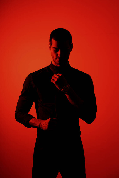 Silhouette of a young confident handsome businessman wearing black shirt in red light - Photo, Image