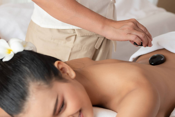 Joven mujer asiática tumbada relajante recibiendo masaje de piedra caliente en el salón de spa. Concepto de tratamiento de belleza. Seleccionar foco mano de masajista
 - Foto, imagen